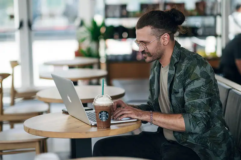 A man smiling at his laptop while sitting in a café